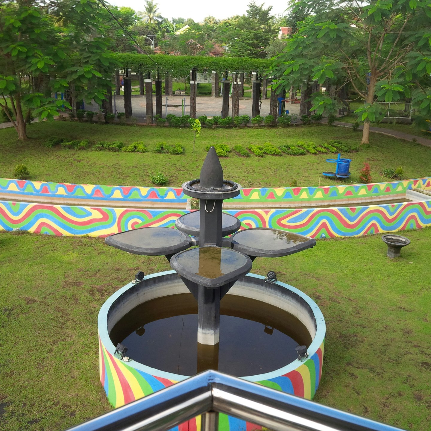 Ein mehrstufiger Betonbrunnen steht in einem grasbewachsenen Park.