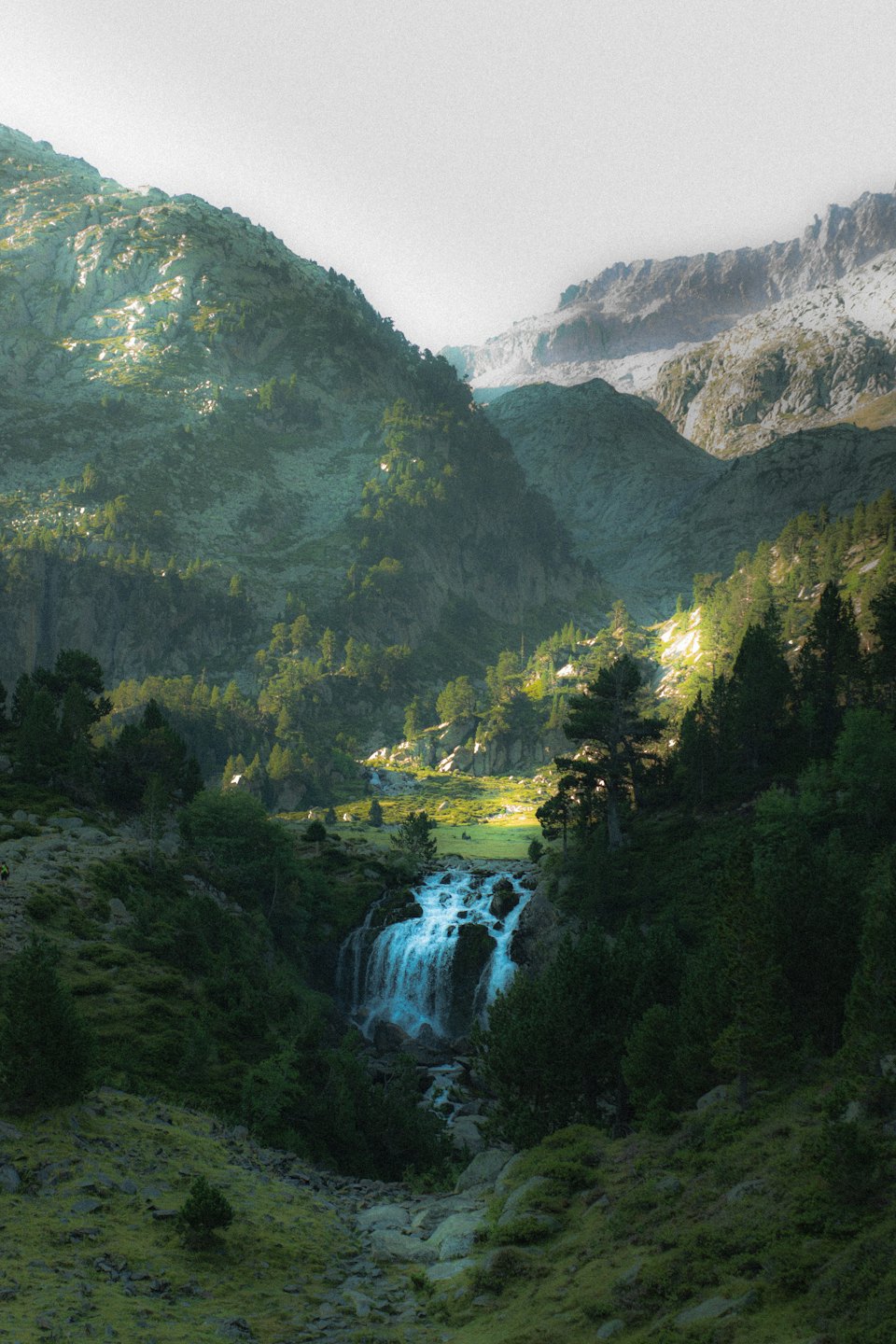 Wasserfall fließt über Felsen in einem Bergtal.