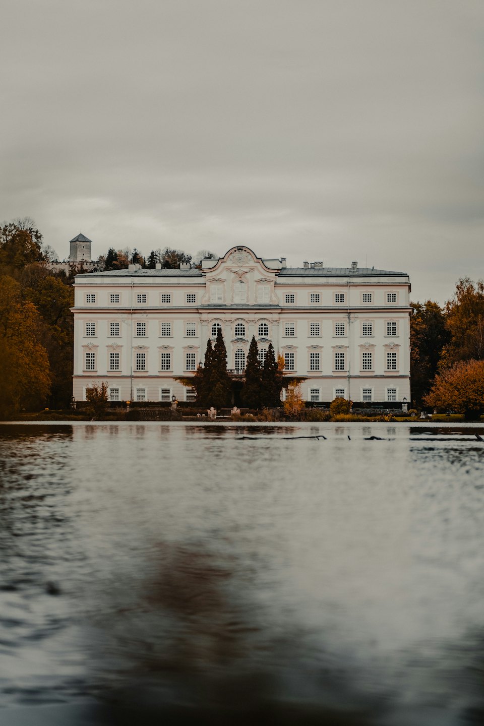 Prunkvoller historischer Palast neben Wasser mit Herbstbäumen.